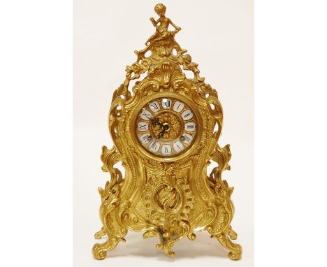 A reproduction Rococo style brass cased mantel clock, the dial having inset porcelain plaques with Roman numerals, eight day 