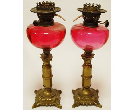 A near pair of pedestal oil lamps each having a cranberry glass reservoir on an associated brass candlestick bases