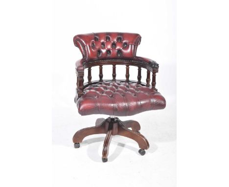 A reproduction oxblood red leather revolving Captain's chairWith a padded back rail supported on turned spindles above a butt