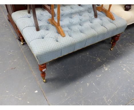 A LARGE BUTTON UPHOLSTERED STOOL ON TURNED LEGS WITH BRASS CASTERS.