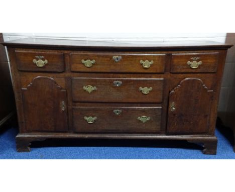 A GEORGIAN OAK DRESSER BASE, having three central graduated long drawers flanked by short drawers over shaped cupboards, all 