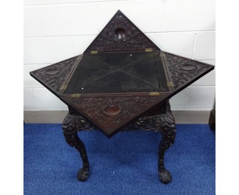 A CARVED ORIENTAL HARDWOOD ENVELOPE GAMES TABLE, having black baize playing surface to centre with relief moulded blossom and