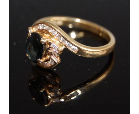 A modern 18ct gold sapphire and diamond cluster ring, arranged as a four claw set oval cut sapphire in a surround of channel 