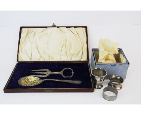 A hallmarked silver egg cup and two silver napkin rings with a silver plated spoon and bread fork.