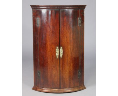 A Georgian mahogany bow-front hanging corner cabinet fitted three shelves enclosed by a pair of panel doors, 70cm wide x 109.