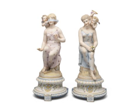 A PAIR OF CONTINENTAL POLYCHROME BISQUE FIGURES, of seated maidens with attendant winged putti, raised on circular socles and