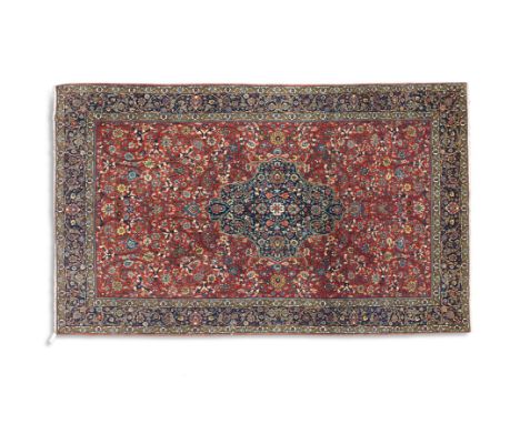 A SEMI-ANTIQUE WOOL RUG, the central field woven with scrolling floral motifs against a brick red ground carpet, enclosed wit