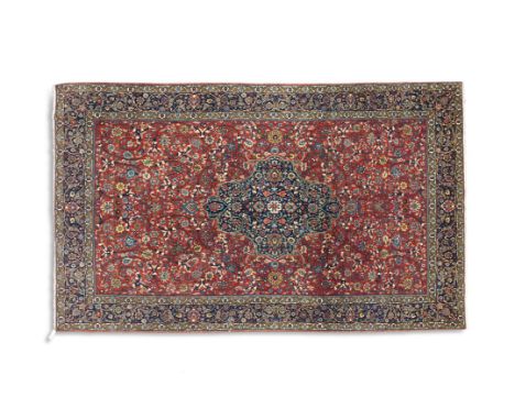 A SEMI-ANTIQUE WOOL RUG, the central field woven with scrolling floral motifs against a brick red ground carpet, enclosed wit