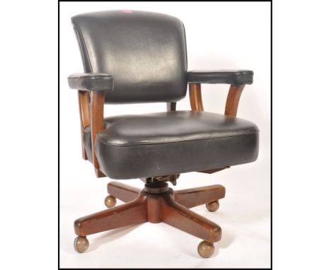 A 1950's retro vintage office desk chair having a thick stuffed black leather seat , backrest and armrests raised on a quadru