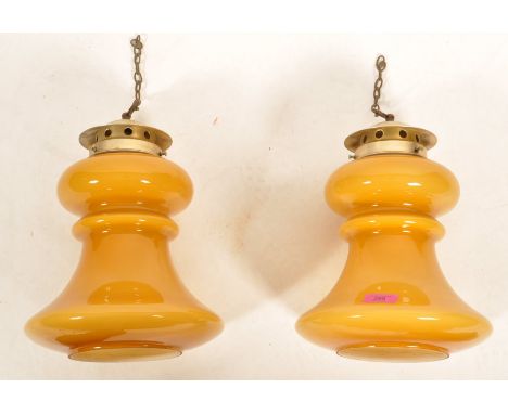 A pair of mid century large amber yellow glass hanging lantern pendant lamps. The cylindrical amber glass shades with bronzed