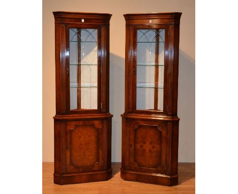 A pair of good reproduction walnut corner cabinets, with glazed door, enclosing glass shelves, above panelled door enclosing 