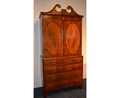 An early 19th century George III style mahogany napery press on chest, with broken swan pediment ending in scrolls above two 