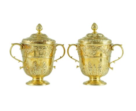 A good pair of George II embossed silver gilt two handled pedestal cups and covers, by Benjamin Gignac, engraved with tarms o