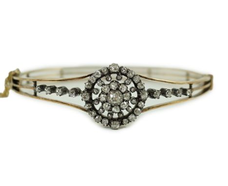 A Victorian gold and diamond cluster set hinged bangle, with central flower head motif, interior diameter approx. 58mm, gross