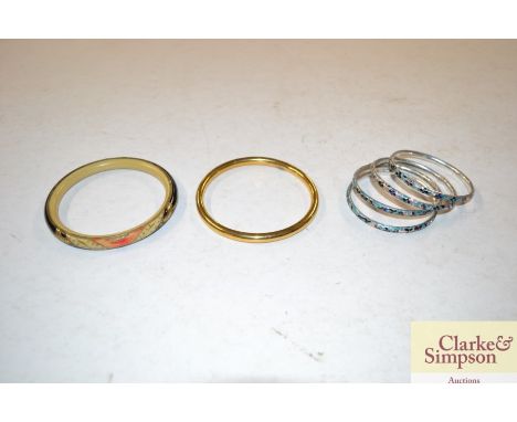 Four white metal and enamel decorated bangles; a rolled gold bangle; and a Bakelite bangle 