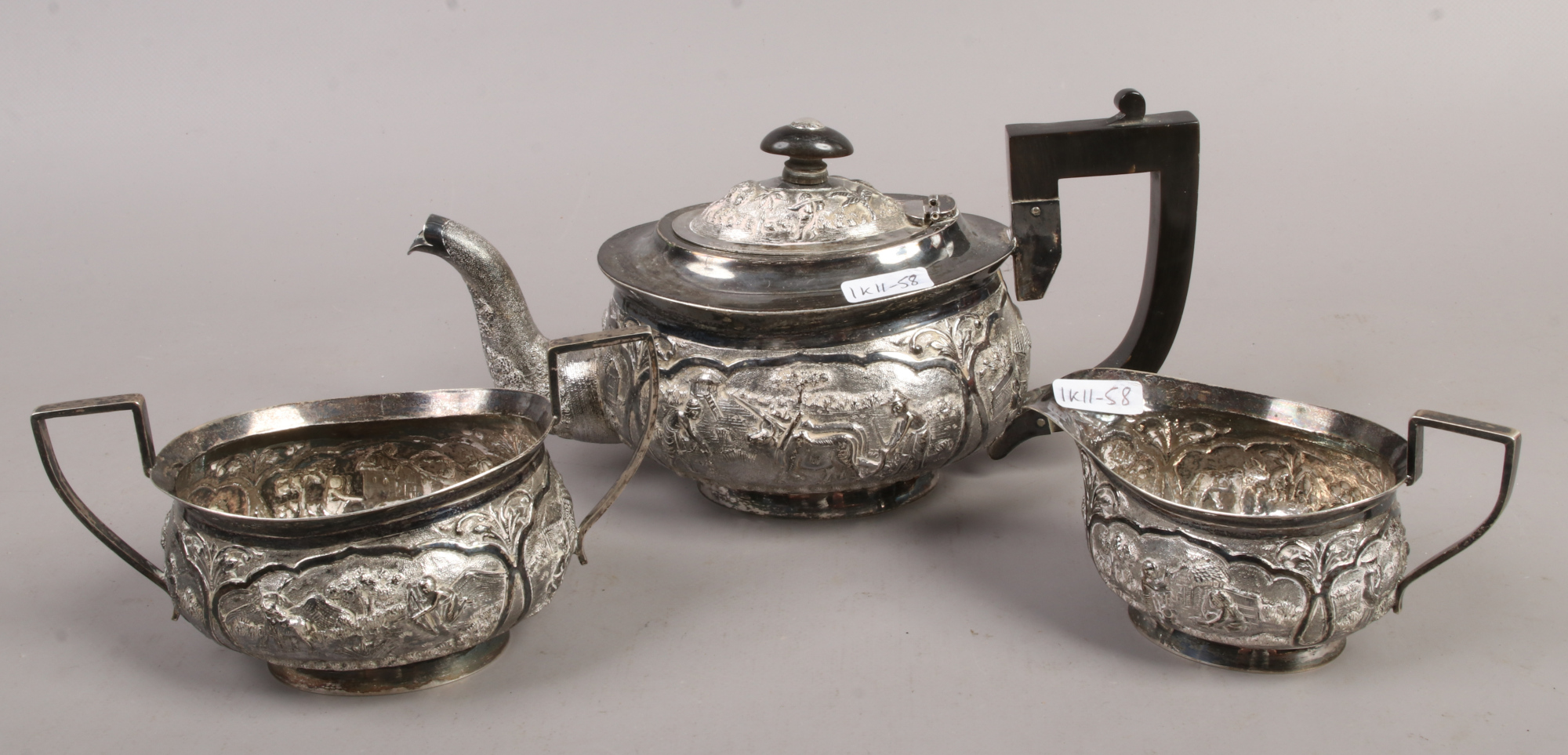 An oriental white metal three piece tea set decorated with landscapes
