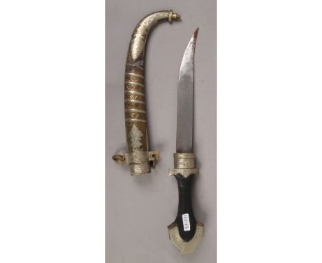 An eastern dagger with ebonised handle and brass and white metal scabbard.