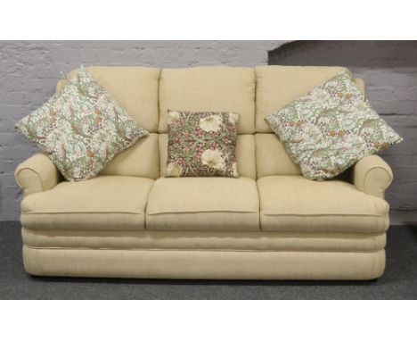 A good quality cream upholstered three seat sofa and matching fireside arm chair with William Morris style cushions.