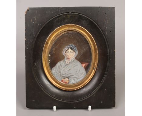 A 19th century ebonised framed hand painted portrait miniature on ivory of a seated old lady reading, dated 1840.
