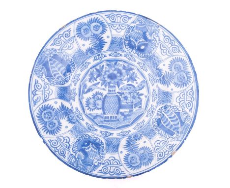A Dutch blue and white delftware charger painted in the Chinese Kraak style with a central vase of flowers, the rim with styl