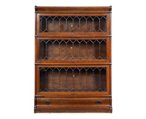 A Globe Wernicke oak three section bookcase, with leaded glazed hinged panel falls and cushion drawer to the plinth base, 87c
