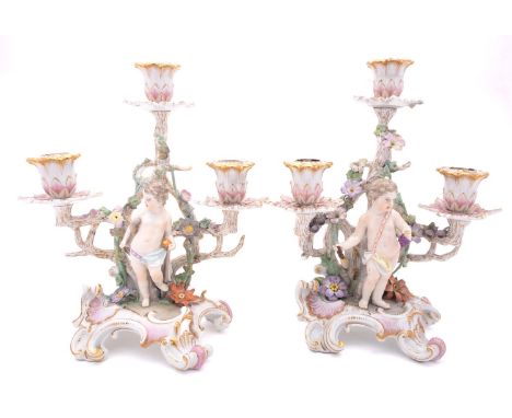 A pair of Berlin [KPM] porcelain three-branch candelabra in the form of putti standing by entwined branches and on rococco ba