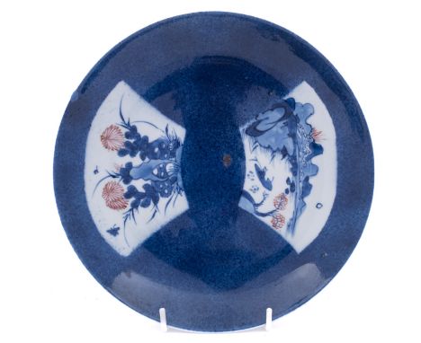 A Chinese underglaze blue and copper-red saucer dish, Kangxi decorated with two fan-shaped panels, one depicting a lake scene