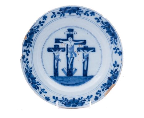 A Dutch delftware crucifixion plate, 18th century painted in blue and iron-red,  the rim with border of flower sprays, 23cm [
