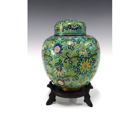 A large Chinese cloisonne ginger jar and cover, with flowers on a green field, 25cm, together with an associated wooden stand