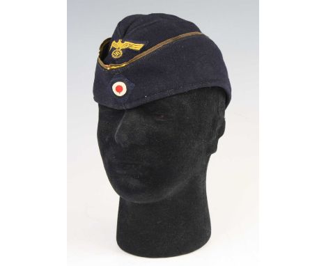 A German Third Reich Kriegsmarine side cap, in blue wool with gold wire piping to the curtain having applied Parteiadler and 