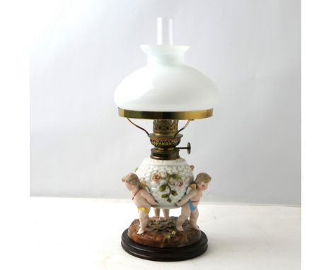 Continental porcelain oil lamp, base supported with three cherubs with original shade and burner