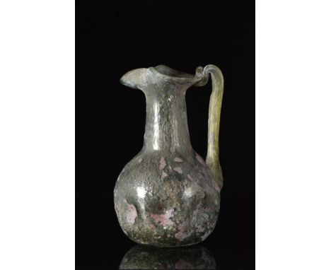 Ca. 200-300 AD.A beautiful, lightly green pitcher standing on a circular, concave base. The pear-shaped body with a decorativ