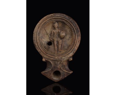Ca. 100-200 AD.A mould-made terracotta oil lamp with concave discus bearing a relief image of a standing, armoured gladiator 