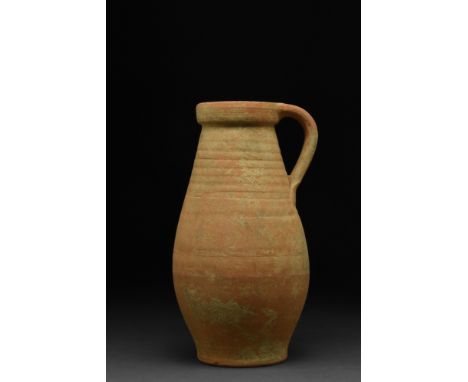 Ca. 200-400 AD.An unglazed ceramic tall piriform jug with spiral wheel-ridging, broad mouth, and a sturdy strap handle connec