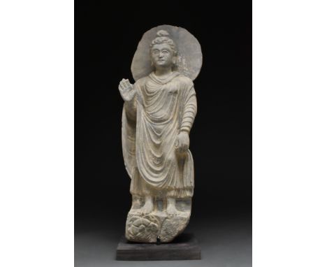 Ca. 200-300 AD.A grey schist figure of a Buddha standing atop a lotus-decorated plinth. This excellent figure is backed by a 