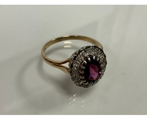 A 9ct yellow and white gold dress ring set with a purplish red rhodolite garnet surrounded by a round cut diamond halo. Oval-