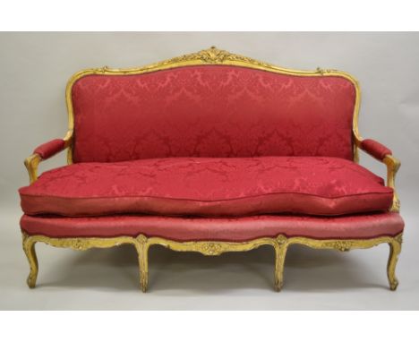 19th Century French carved and gilded three seat salon sofa, upholstered in crimson damask with scroll arms above a serpentin