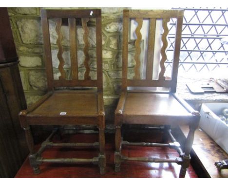 A pair of old English style oak side chairs with solid seats, the stick backs with wavy moulded outline raised on turned supp