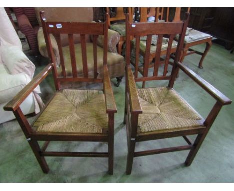 A pair of arts and crafts oak elbow chairs with vertical stick backs and sea grass seats