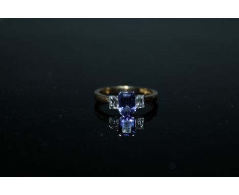 A HALLMARKED 18 CARAT GOLD TANZANITE AND DIAMOND RING, set with a central emerald cut tanzanite of approx 0.94 carat with a e