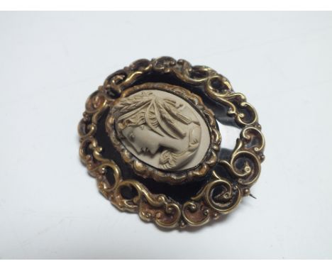 A VICTORIAN CARVED LAVA MEMORIAL BROOCH, of oval form with black enamel and scrolling yellow metal border, having central car