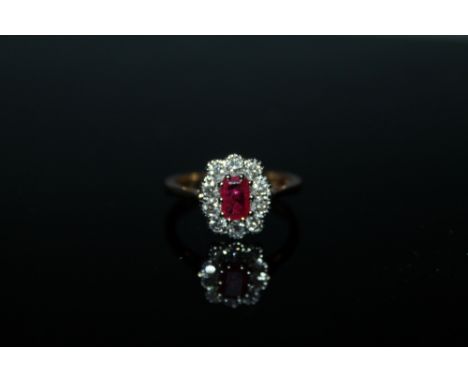 AN 18 CARAT GOLD RUBY AND DIAMOND RING, the central emerald cut ruby being of approx 0.75 carat is surrounded by brilliant cu