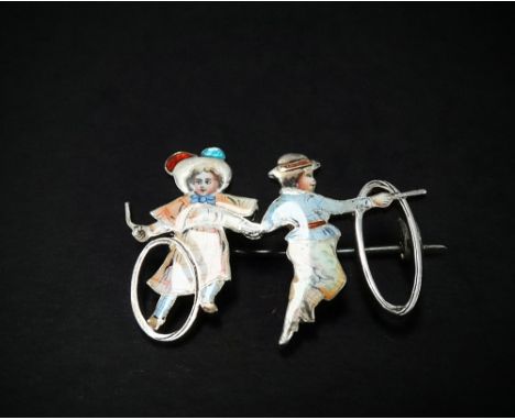 A French 900 silver and coloured enamel brooch in the form of an early 20th century girl and boy playing with hoop and sticks