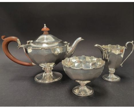 A George V silver three piece batchelor tea set of faceted pedestal form with crenallated edge, maker Edward Souter Barnsley 