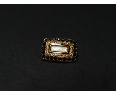 A George IV 18ct. gold mourning brooch set with black stones around a hair panel with black enamel border, the back with insc