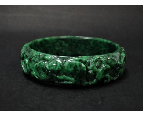 A mottled green jade bangle, carved with two rabbits amongst leaf scrolls, diameter 7.5cm.