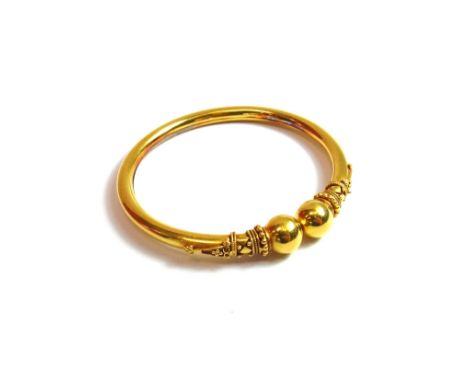 A gold bangle, of sprung circular form, with applied bead and wirework decoration and with larger bead terminals in the class