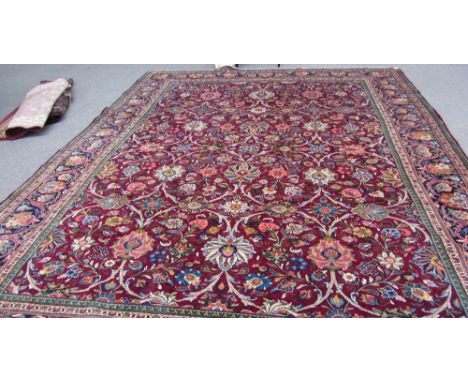 A Kashan carpet, Persian, the burgundy field with an allover design of bold palmettes, curved vines and floral sprays, a dark