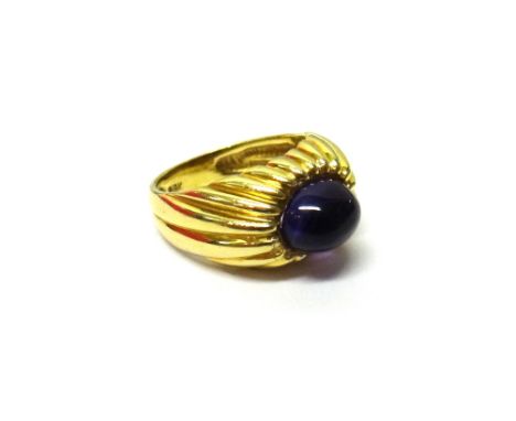 A gold and cabochon amethyst set single stone ring, mounted with an oval cabochon amethyst and otherwise in a ridged design, 