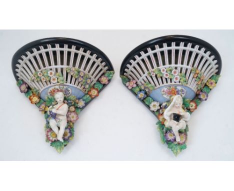 A pair of German porcelain wall brackets, 19th century, of pierced trellis design with encrusted flowers terminating in putti